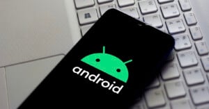 A smartphone displays the green Android logo and the word "android" on its screen, resting on a silver laptop keyboard.