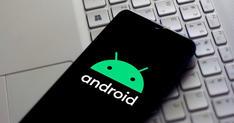 A smartphone displays the green Android logo and the word "android" on its screen, resting on a silver laptop keyboard.