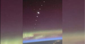 A view of the Orion constellation shining brightly above Earth, with the green and purple hues of an aurora and Earth's thin blue atmosphere visible below.