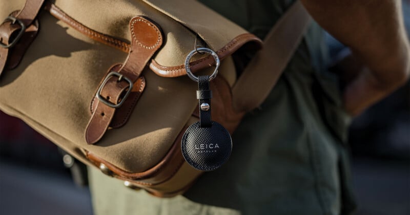 Primer plano de un bolso de cuero y lona color canela con un llavero redondo negro marcado 