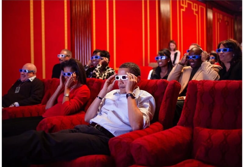 A group of people sit in red armchairs in a theater with bright red walls, all wearing 3D glasses and watching a movie.