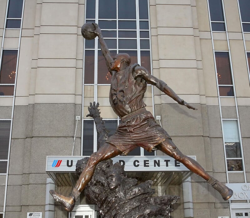 A bronze statue of a basketball player soaring mid-air with an outstretched arm holding a basketball, located in front of the United Center building.