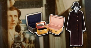 A vintage photo of a woman with a camera is in the background. In the foreground are three vintage suitcases, one open with a red interior, and a long, dark brown coat with gold buttons and a black hat on a mannequin.