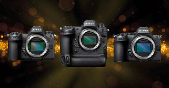 Three Nikon mirrorless cameras are displayed side by side against a dark background with golden bokeh lights. The camera in the middle is larger and has a vertical grip, while the other two are more compact.