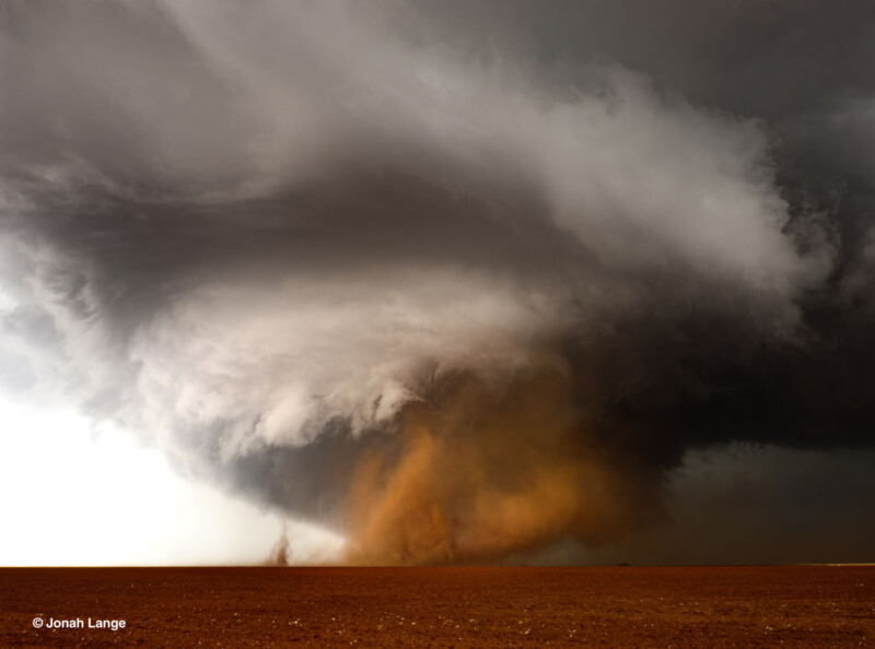 Una enorme y arremolinada nube de tormenta con un denso embudo negro descendió sobre la tierra plana de color marrón rojizo, levantando polvo y escombros bajo un cielo espectacular.