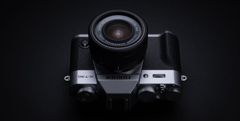 A Fujifilm X-T30 camera with a Fujinon lens is shown from above on a dark background, highlighting its retro-inspired design and control dials.