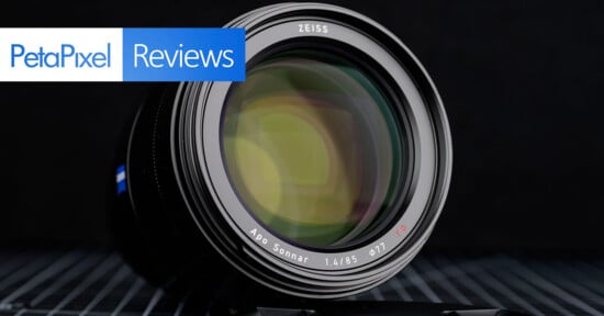 Close-up of a Zeiss Apo Sonnar 85mm f/1.4 camera lens with "PetaPixel Reviews" text overlay in the top left corner, set against a dark background.