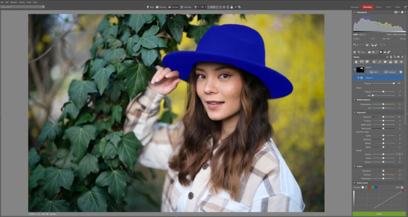 A woman wearing a bright blue hat and a plaid shirt stands outdoors next to green ivy, smiling at the camera. The background is blurred with yellow and green tones. Editing software interface is visible around the photo.
