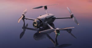 A close-up of a modern quadcopter drone with a camera, resting on a reflective surface under a pink and blue sky at dusk.