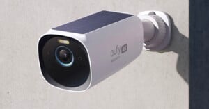 A white Eufy 4K security camera with a solar panel on top is mounted on an exterior wall, facing forward to monitor the area.