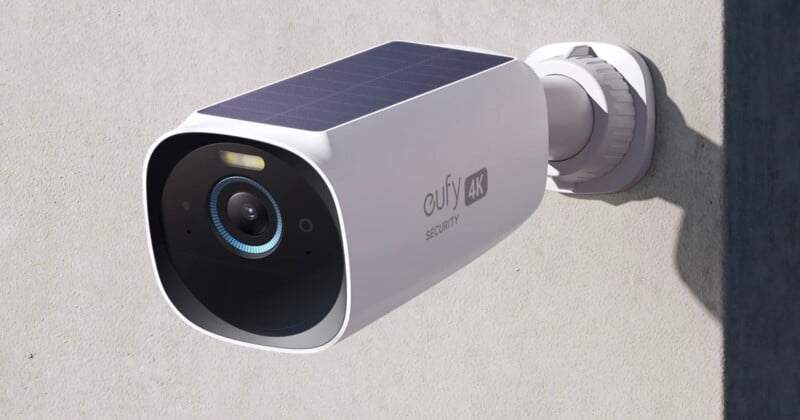 A white Eufy 4K security camera with a solar panel on top is mounted on an exterior wall, facing forward to monitor the area.