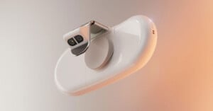 A sleek, modern white device with smooth curves and a metallic dual-lens camera attachment, floating against a gradient background of light gray and warm beige tones.