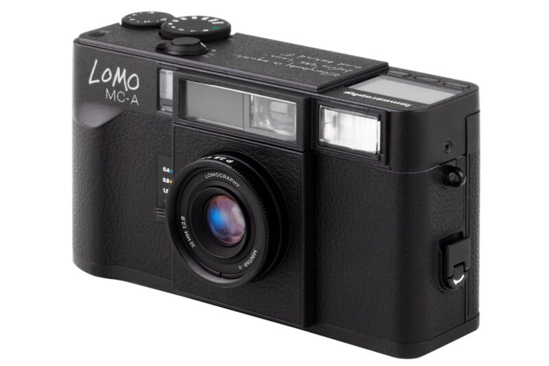 A black LOMO MC-A film camera with a prominent lens, viewfinder, and various control dials, shown angled on a white background.