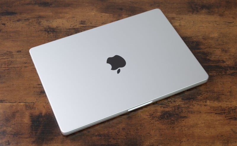 A closed silver MacBook with an Apple logo sits on a wooden table.