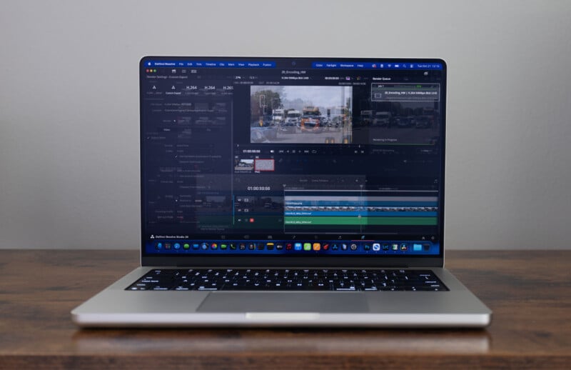 A laptop on a wooden desk displays video editing software with a timeline and preview of traffic footage. The screen shows multiple layers and editing tools. The background is plain and light-colored.