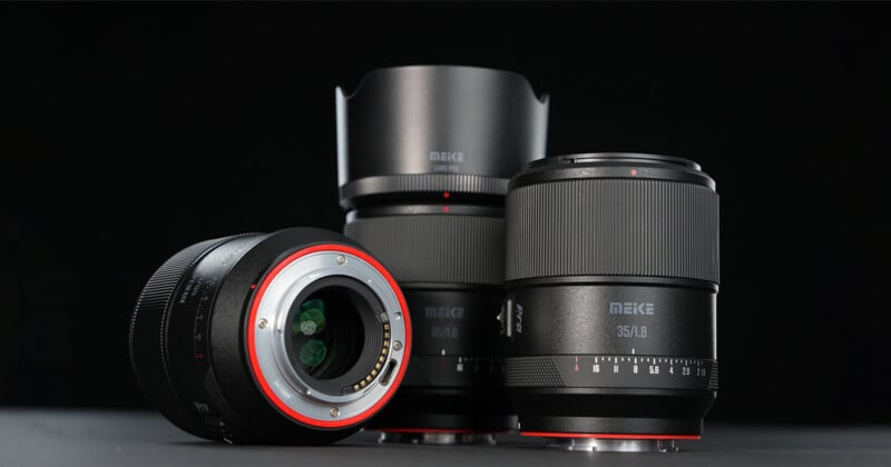 Tres lentes de cámara Meike se muestran en la superficie oscura sobre un fondo negro. Una lente se acuesta para mostrar la montura, mientras que los otros dos están erguidos, acentuando su anillo de enfoque y marca texturizados.