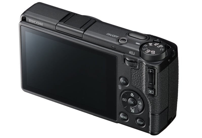 A digital Ricoh camera shown from the back, displaying its large screen, control buttons, dials, and textured grip.