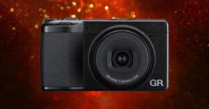A black compact digital camera with a GR lens is centered against a red background with glowing bokeh lights.