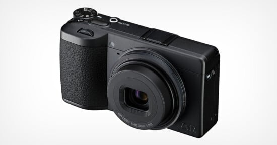 A black compact digital camera with a textured grip, labeled "GR" on the front, featuring a prominent lens and control dials on top, photographed against a plain white background.