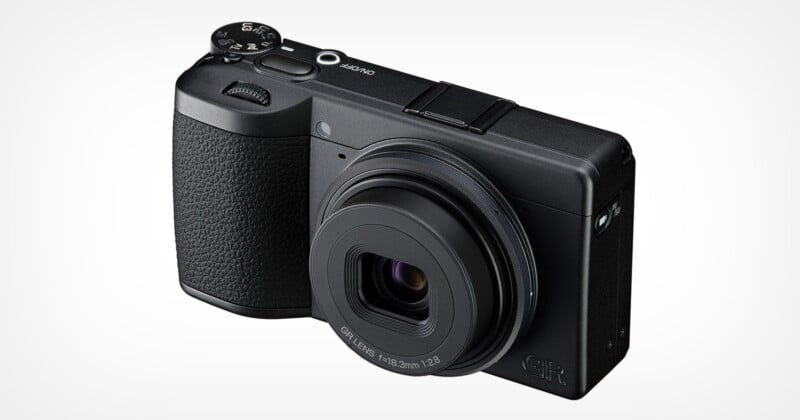 A black compact digital camera with a textured grip, labeled "GR" on the front, featuring a prominent lens and control dials on top, photographed against a plain white background.
