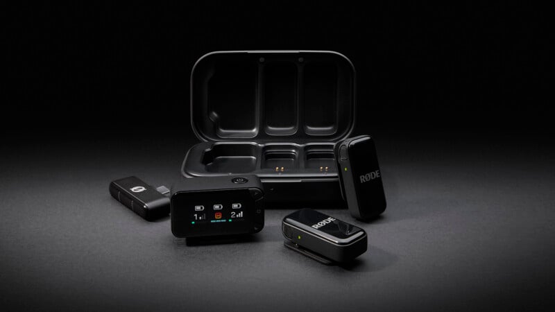 A set of wireless microphone equipment, including a charging case, transmitters, and receivers with "RODE" branding, displayed on a dark surface with soft lighting.