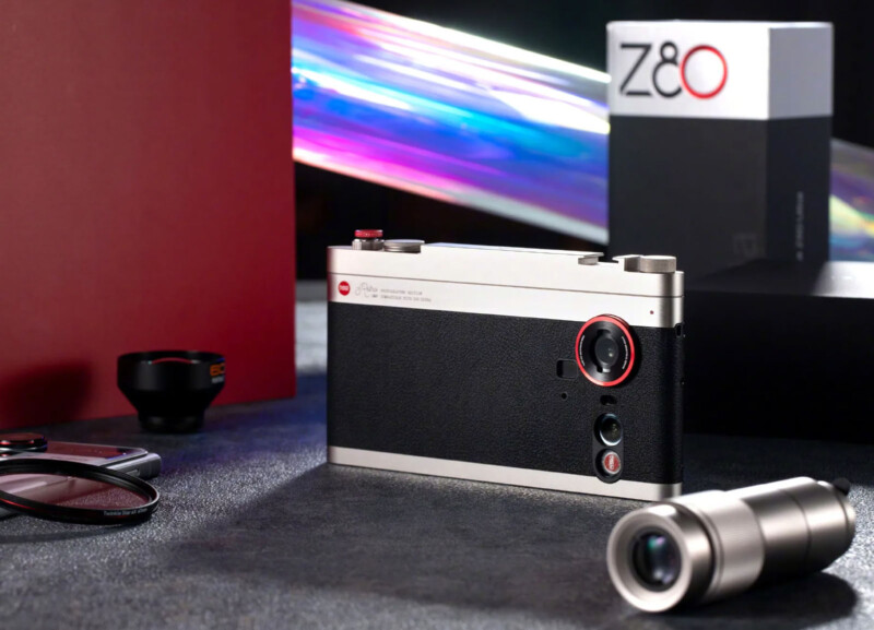 Sobre la mesa se muestra una moderna cámara digital compacta con acabado negro y plateado, rodeada de accesorios para la cámara y una caja etiquetada. "Z8o." Al fondo aparecen rayos de luz de colores.