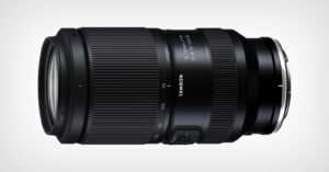 A black Tamron camera lens with zoom and focus rings, labeled "70-180mm F/2.8 Di III VXD," lying horizontally on a light background.