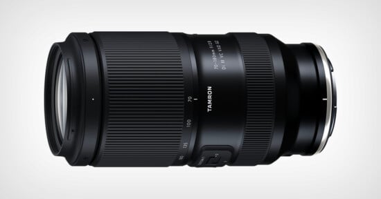 A black Tamron camera lens with zoom and focus rings, labeled "70-180mm F/2.8 Di III VXD," lying horizontally on a light background.