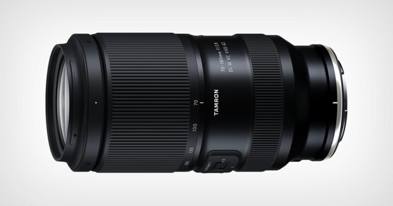 A black Tamron camera lens with zoom and focus rings, labeled "70-180mm F/2.8 Di III VXD," lying horizontally on a light background.