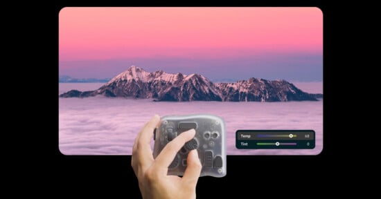 A hand adjusts a translucent editing device in front of a screen displaying snow-capped mountains above clouds at sunset; temperature and tint sliders are visible on the image.