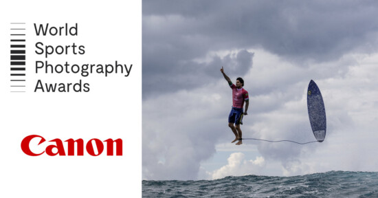 A surfer wearing a pink shirt appears to be mid-air above the ocean, with his surfboard flying nearby. The sky is cloudy. The left side features the text "World Sports Photography Awards" and the Canon logo.