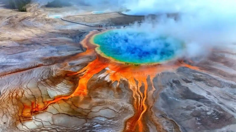 Una vista aérea del Gran Manantial Prismático en el Parque Nacional de Yellowstone, que muestra anillos de vivos colores azul, verde, amarillo y naranja rodeados de vapor y espectaculares depósitos minerales.