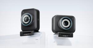 Two black rectangular webcams with circular blue accents are mounted on top of white computer monitors. The brand "YoloLiv" is visible on each webcam's base. The background is plain and light-colored.