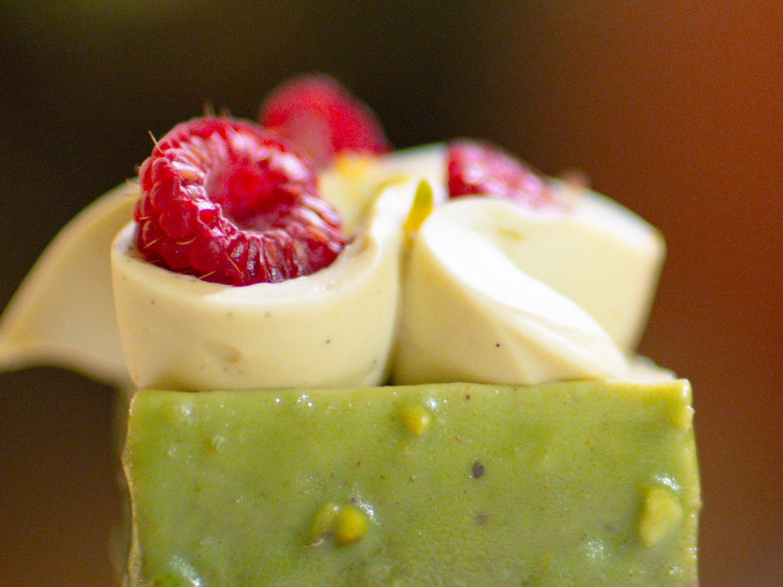 Primer plano de una barra de postres verde con remolinos blancos cremosos y frambuesas frescas con fondo borroso.