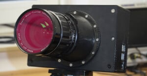 Close-up of a custom-built digital camera with a large Super-Multi-Coated Takumar lens attached, mounted on a tripod, with visible screws and USB ports on the camera body.