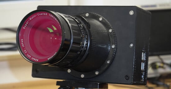 Close-up of a custom-built digital camera with a large Super-Multi-Coated Takumar lens attached, mounted on a tripod, with visible screws and USB ports on the camera body.