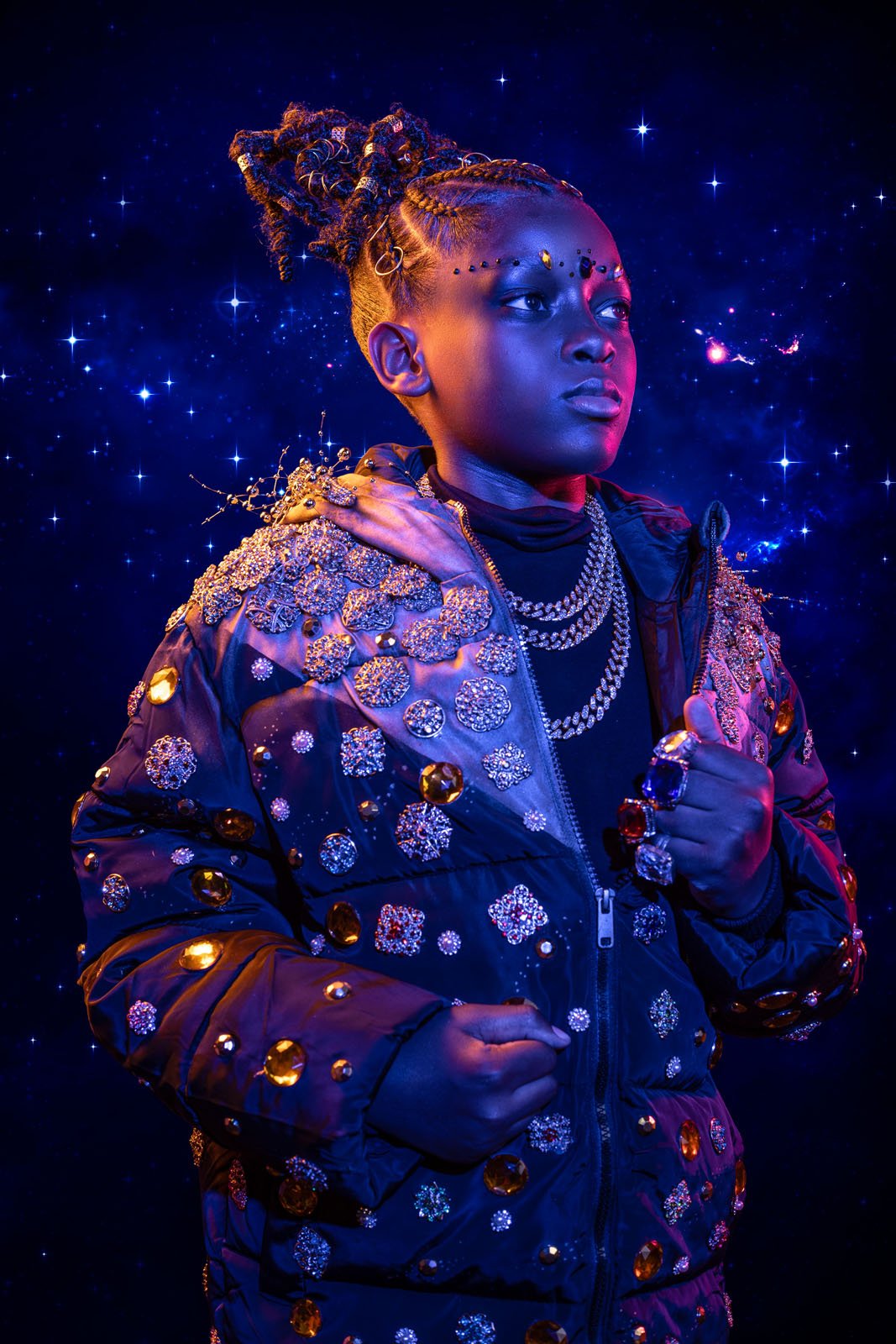 Un hombre con la cara pintada de azul oscuro se alza contra un fondo de cielo estrellado, vestido con una chaqueta enjoyada, collares y anillos en capas, adornado con cabello y una iluminación espectacular, acentuando el estilo cósmico futurista.