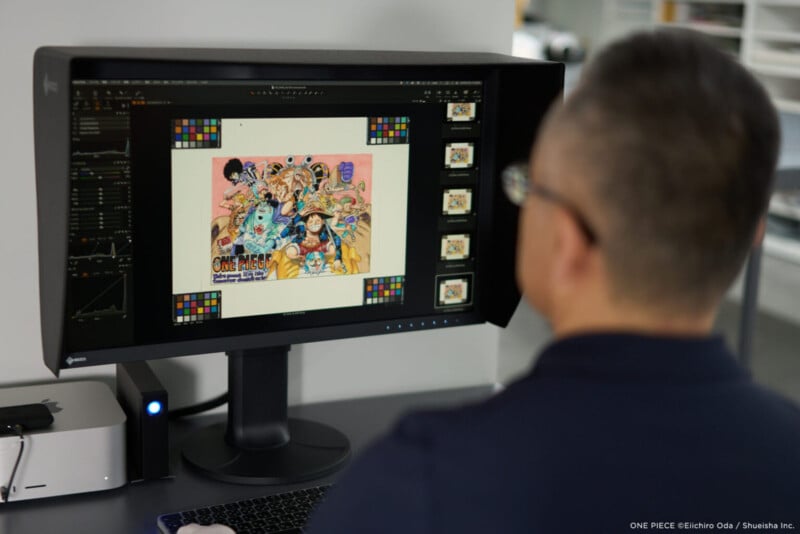 Un hombre con pelo corto y gafas mira un monitor que muestra coloridas ilustraciones de anime. "una pieza," Cuenta con múltiples personajes y gráficos de estilo cómic. La pantalla también muestra herramientas de calibración de color.