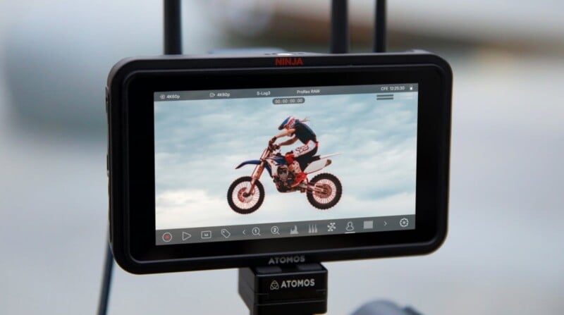 El monitor muestra un vídeo de una persona montando una moto de cross contra un cielo nublado, con varios controles de reproducción visibles en la pantalla.