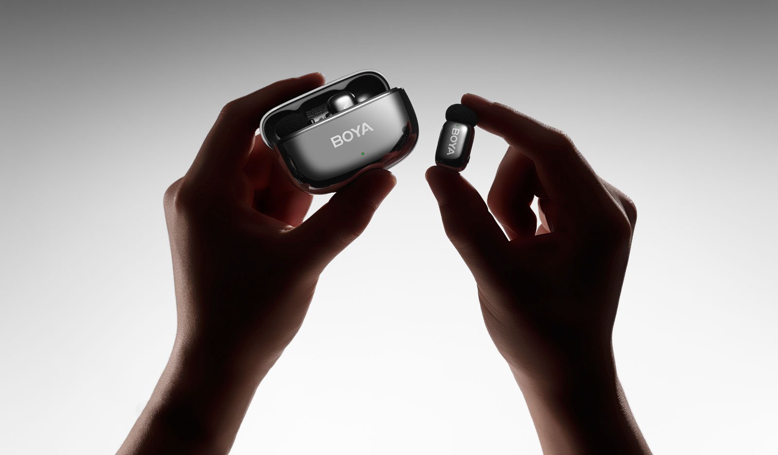 Two hands holding a pair of BOYA wireless earbuds, with one hand holding the open charging case and the other holding a single earbud against a white background.