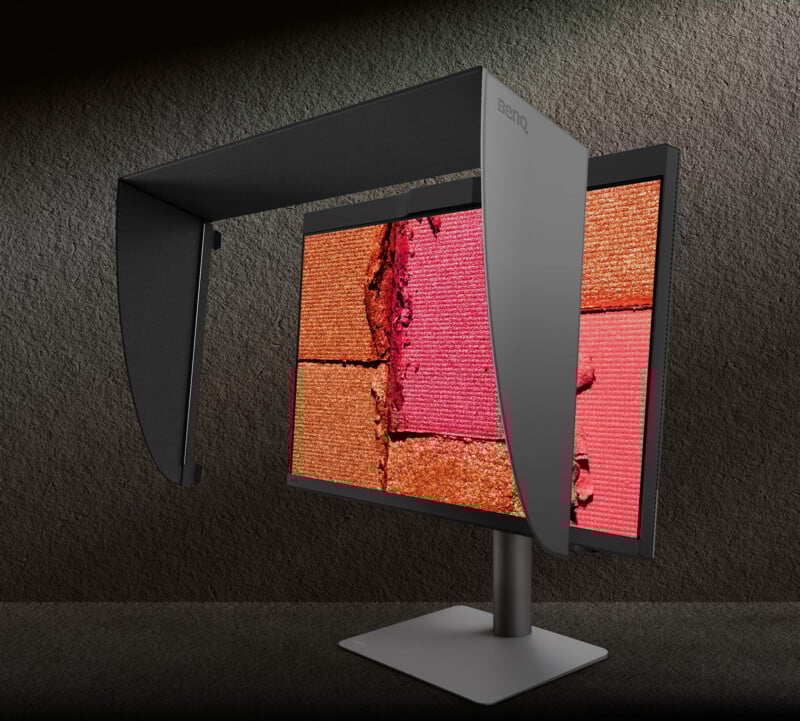 Monitor de computadora BenQ con capota sobre soporte de metal que muestra una imagen de una superficie texturizada de color rojo anaranjado que se asemeja a la tierra agrietada y que contrasta con un fondo de textura oscura.