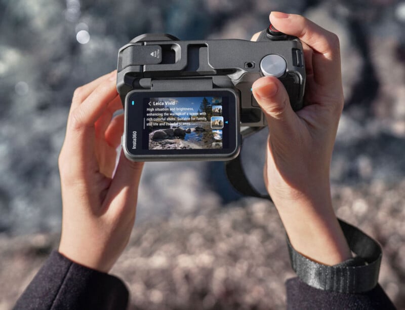 Una persona sostiene una cámara digital y mira una pantalla que muestra una fotografía de un paisaje y una descripción de texto. "Leica es vívida." La escena del fondo parece al aire libre y está ligeramente borrosa.