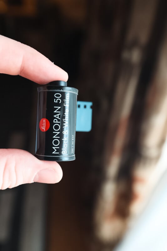 A hand holding a roll of Leica MONOPAN 50 black and white film, with a blurred background.