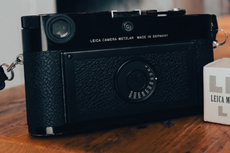 A black Leica Camera Wetzlar sits on a wooden surface next to a white Leica box. The camera’s textured body and dials are clearly visible, with “Made in Germany” engraved on the top.