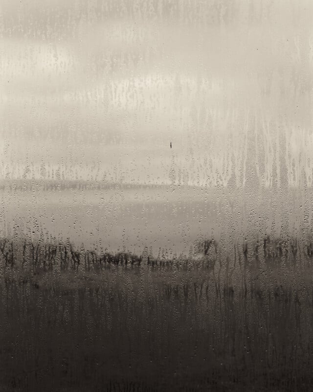 El paisaje brumoso y borroso que se ve a través de la ventana está cubierto de condensación, con gotas y rayas que oscurecen la vista de los árboles distantes y el horizonte.
