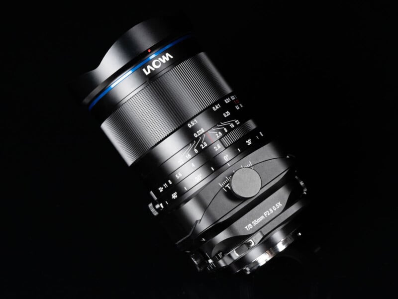 A close-up photo of a Laowa camera lens with detailed focus and aperture markings, set against a black background. The lens features a blue ring and the text "15-35mm F2.8-3.5X" is visible.