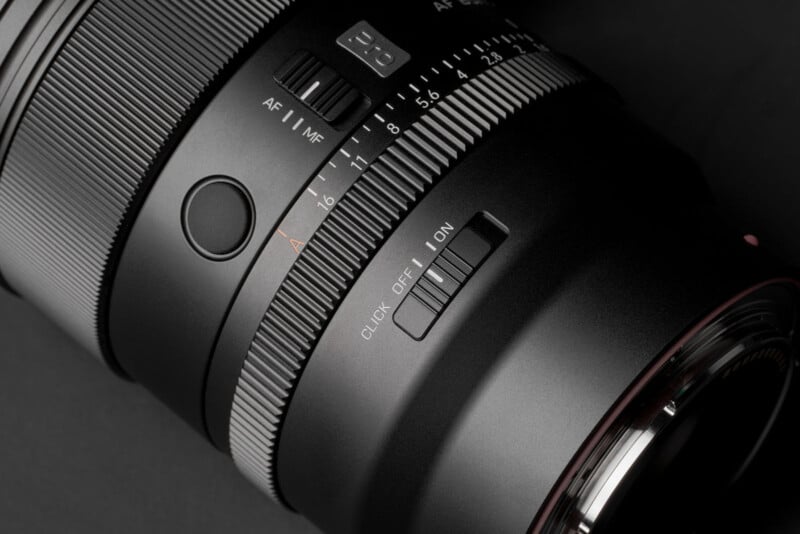 Primer plano de la lente de la cámara que muestra marcas detalladas de enfoque y apertura, así como interruptores marcados "Enfoque automático/enfoque manual" y "Haga clic en Cerrar/Abrir," Sobre un fondo oscuro.