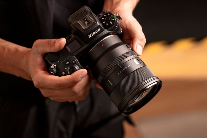 Un hombre que sostiene una cámara digital Nikon con una lente de zoom grande, centrándose en las manos y la cámara sobre un fondo borroso.