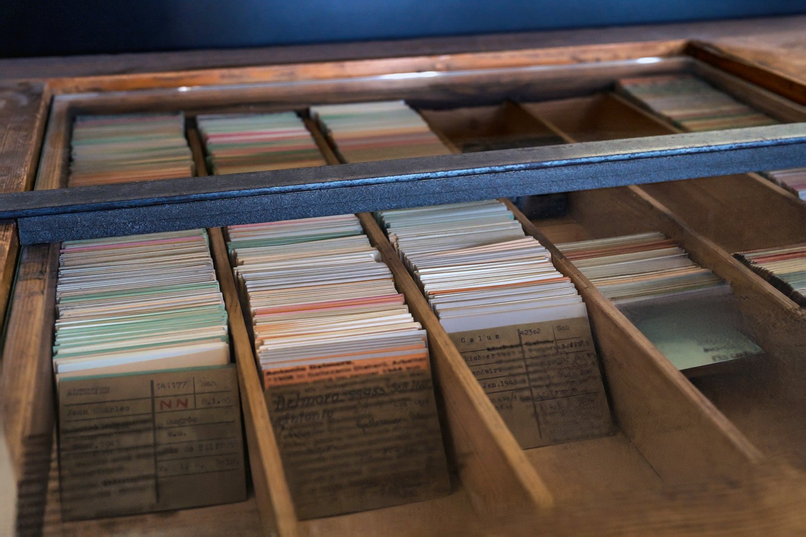 A wooden drawer filled with organized index cards, separated by wooden dividers. Some cards have handwritten text, and others are blank or have faded writing. The drawer is viewed from above.