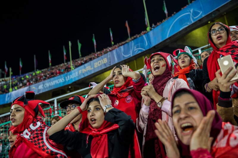 A group of passionate football fans, mostly women wearing red scarves and jerseys, react with excitement and tension in a crowded stadium during the 2018 AFC Champions League Final.